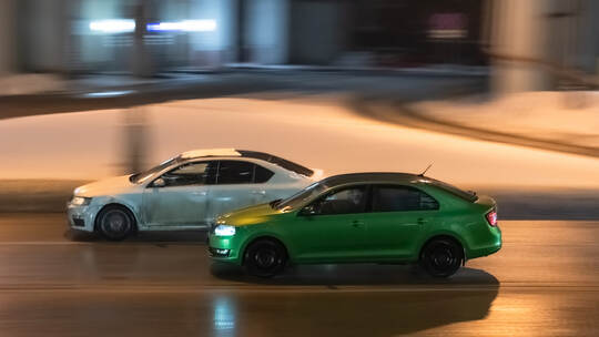 Two cars in motion on city street at night. Racing at high speed on public road. White and green sedans drive on wet winter road