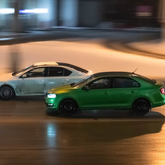 Two cars in motion on city street at night. Racing at high speed on public road. White and green sedans drive on wet winter road