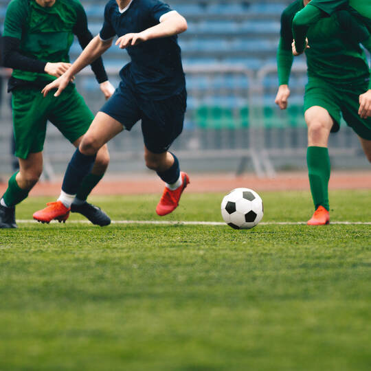 Soccer players run a game and kick soccer ball. European football competition match between players in green and blue uniforms.