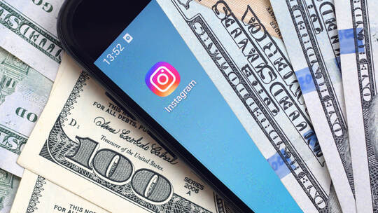Smartphone screen with Instagram app and lot of hundred dollar bills. Business and social networking concept