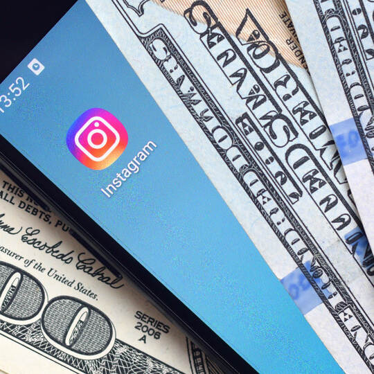 Smartphone screen with Instagram app and lot of hundred dollar bills. Business and social networking concept
