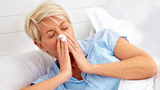 Blowing nose, couple or sick old woman in bed with husband with flu virus, cold or health problem. Sneeze, mature or senior pers