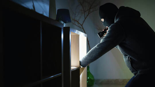Masked robber with flashlight torch checking apartment.