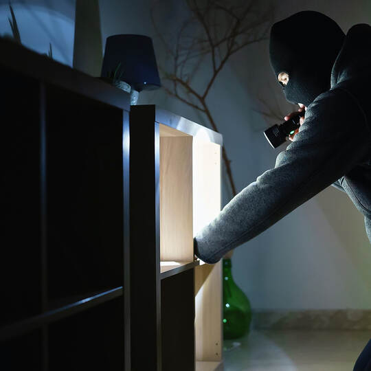 Masked robber with flashlight torch checking apartment.