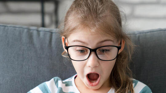 Child looking at mobile phone at home. Kid using smartphone for distance learning, online education. Girl playing games. Technol