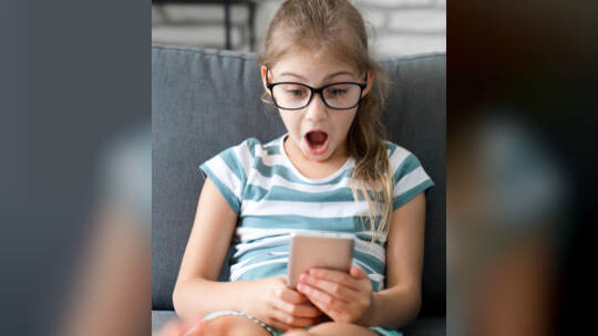 Child looking at mobile phone at home. Kid using smartphone for distance learning, online education. Girl playing games. Technol