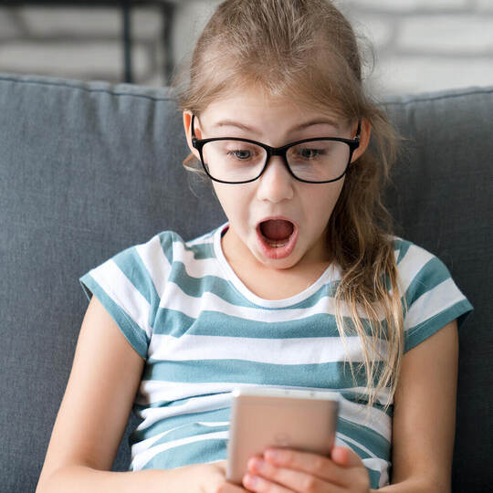 Child looking at mobile phone at home. Kid using smartphone for distance learning, online education. Girl playing games. Technol