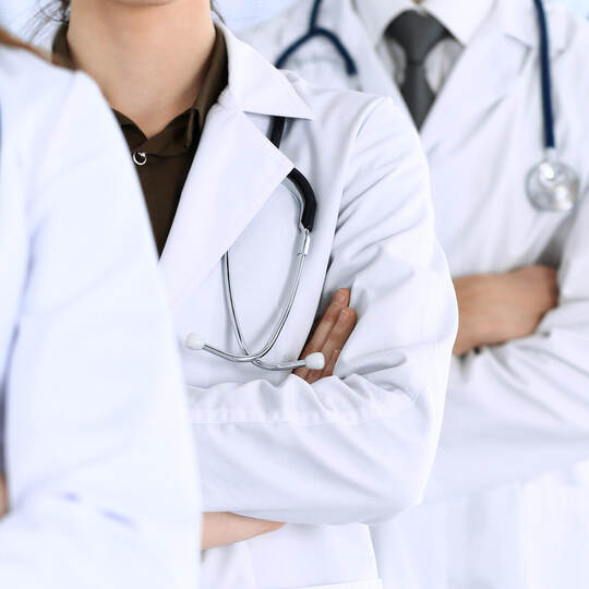 Group of modern doctors standing as a team with arms crossed in hospital office. Physicians ready to examine and help patients.