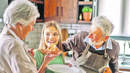 Happy family with grandparent and child in kitchen eating pizza