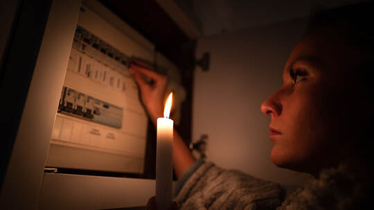 Woman checking fuse box at home during power outage or blackout. No electricity concept