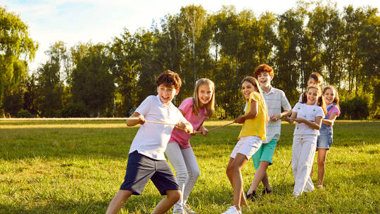 Group of happy kids having fun and playing tug of war in summer camp on vacation